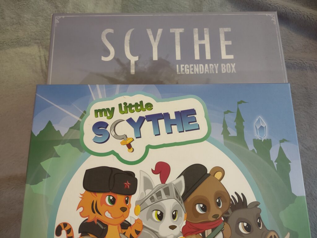 picture shows a large gray box labeled Scythe: Legendary Box underneath a box that says My Little Scythe with colorful animals on the box.